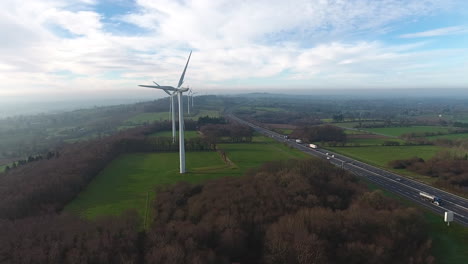 Flying-around-wind-turbines-along-a-highway,-morning-drone-shot